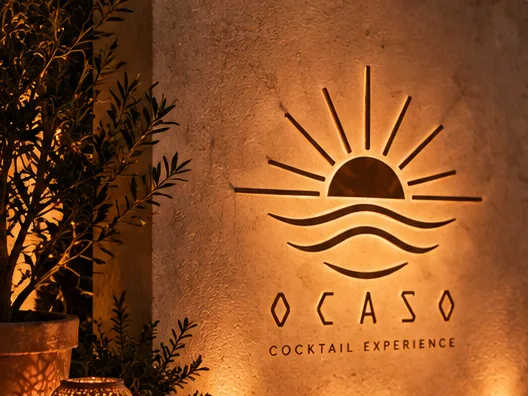 El logotipo iluminado sobre un muro de piedra, entre plantas.